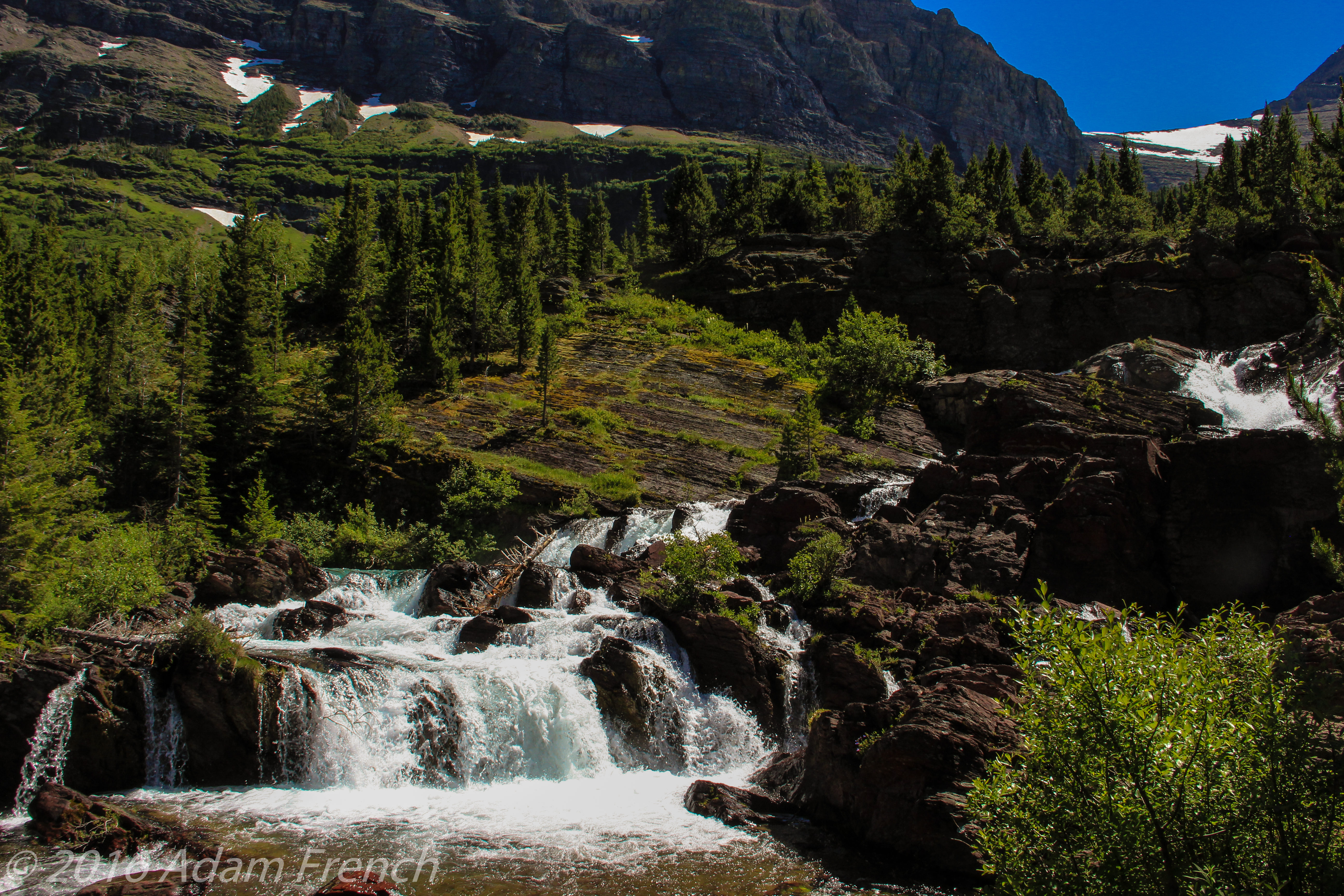 A short waterfall surrounded by pine tree-covered mountainsides