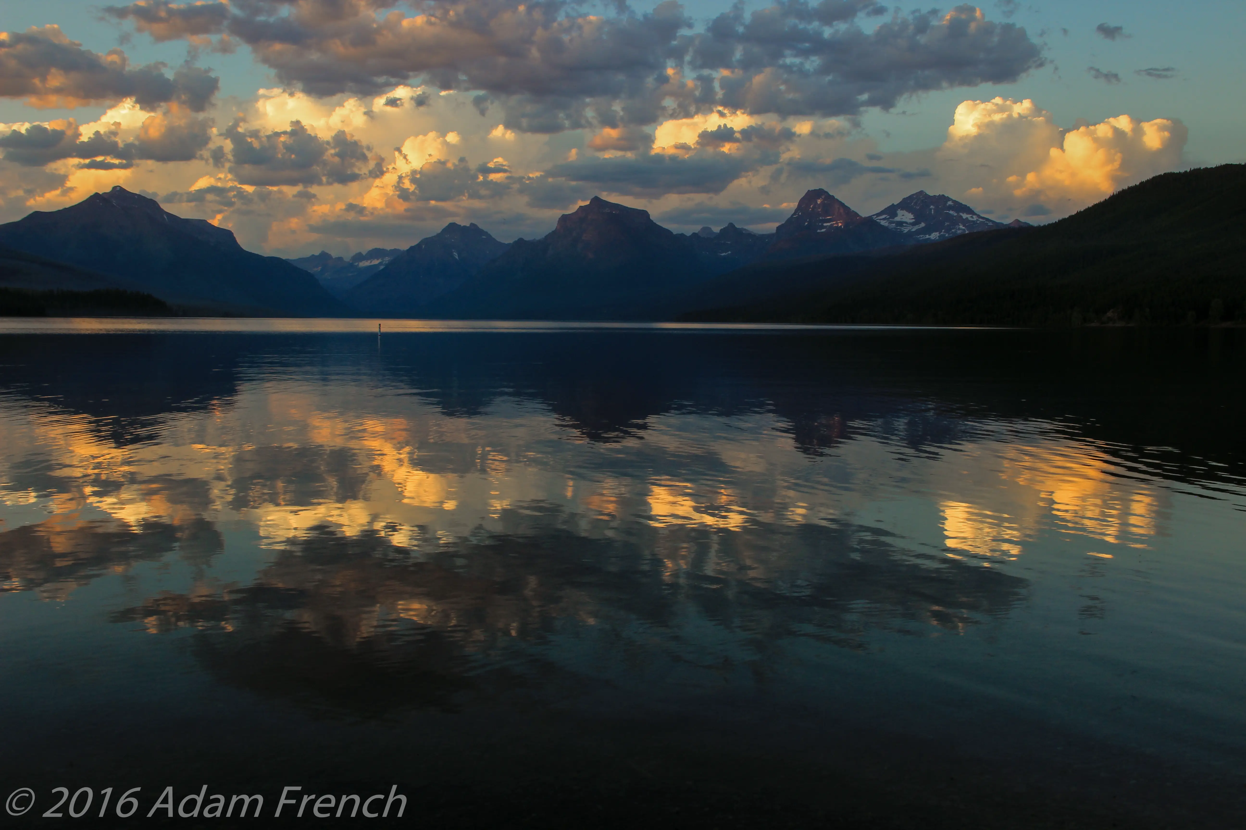 Sunset photo of a flat-water lake with the dark silhouettes of the surrounding mountains and sunset colors in the clouds reflecting in the water