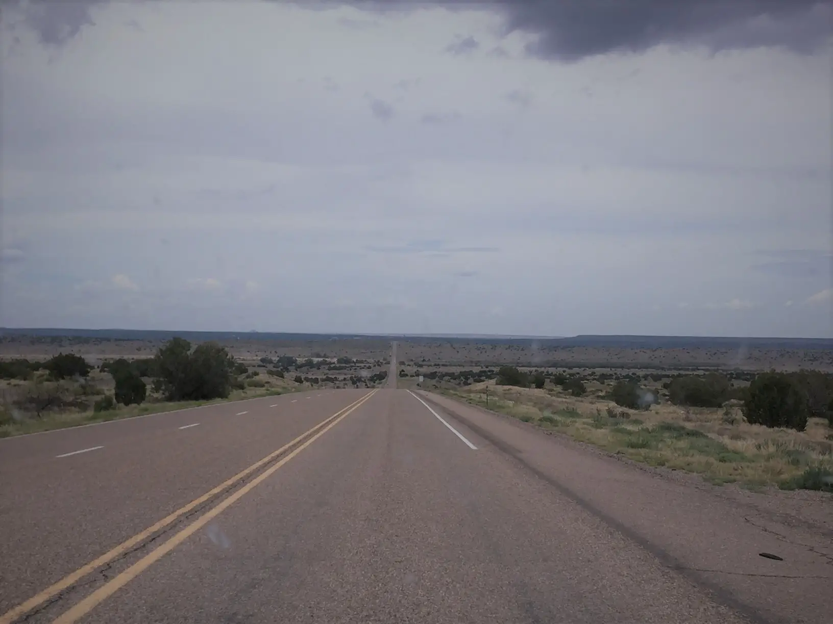 A two-lane, paved road stretches to the horizon amidst desolate, desert scrubland