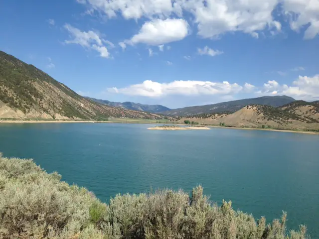 Lake surrounded by scrub brush and tree-covered mountains