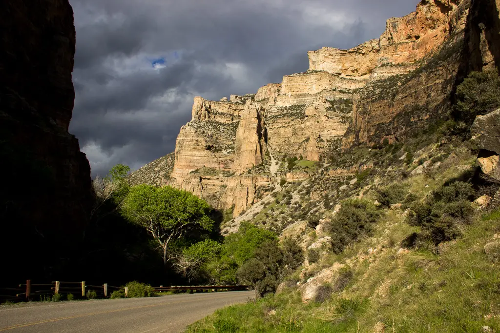 A paved road meanders through rocky, canyon walls with green grass and trees interspersed throughout