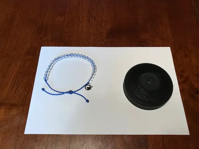 A blue bracelet with clear beads sits next to a water bottle lid to compare for size 