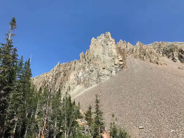 A rocky, craggy mountain with one side a scree slope. Trees are in the foreground