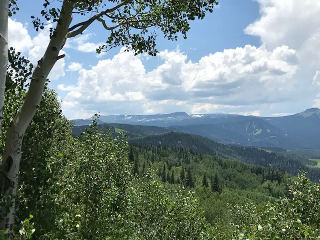 Green, tree-covered mountains spread to the horizon. Spots of snow can be seen on the highest peaks in the far-background