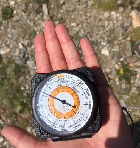 Hand holding an analog dial showing a little over 11,000 feet elevation
