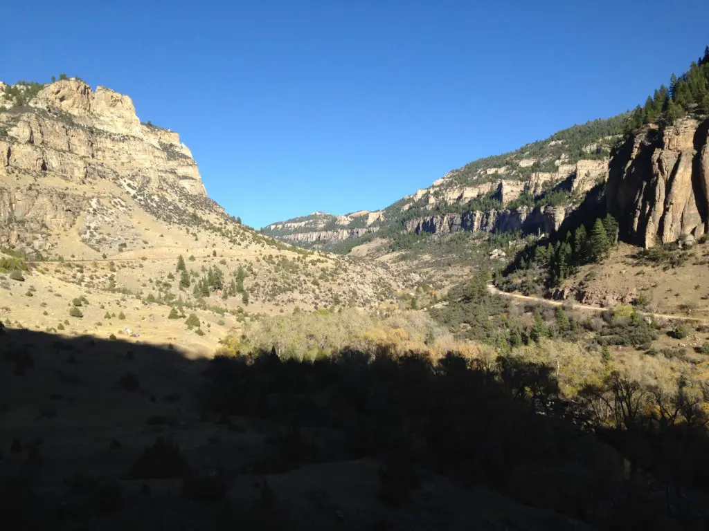 View up a brown rock canyon dotted with trees, all under a clear, blue sky