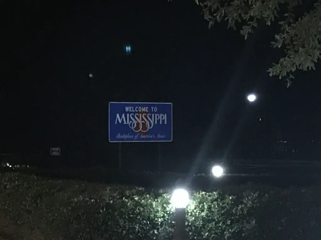 A "Welcome to Mississippi" road sign is lit up in the dark