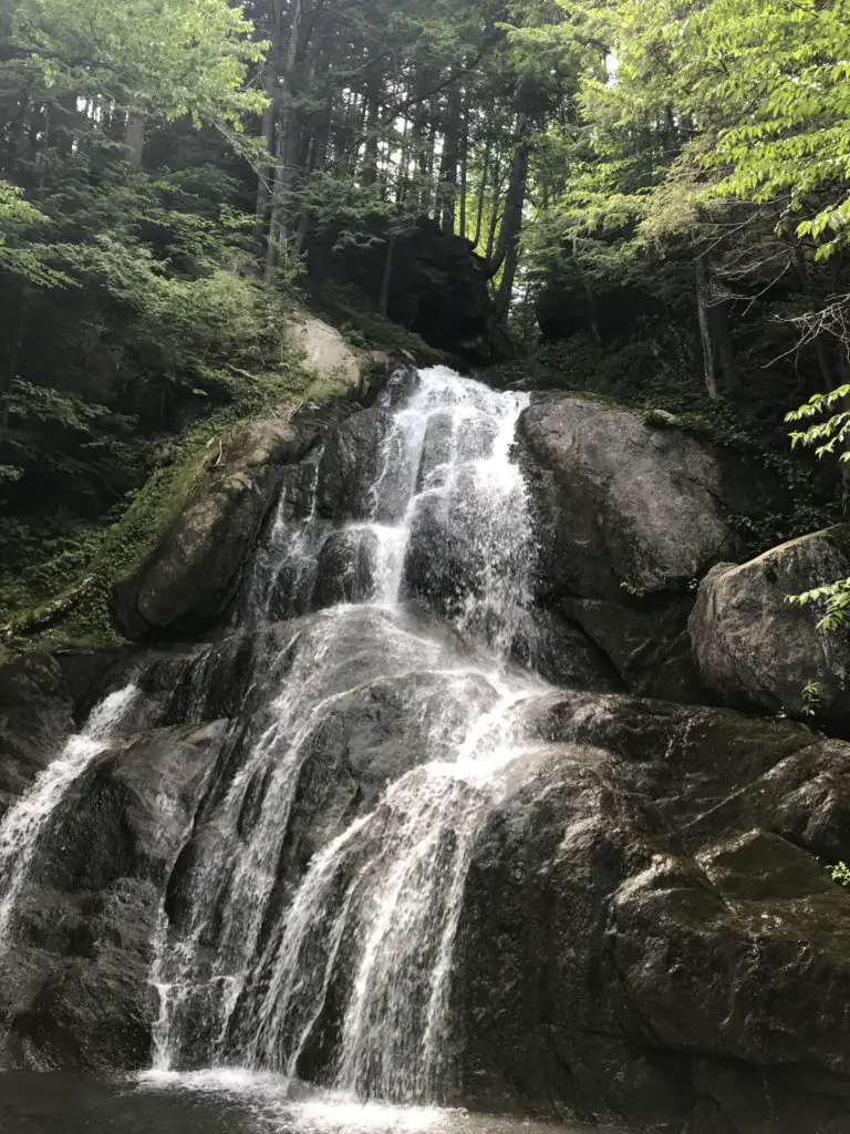 A waterfall over rocks landing in a pool at the bottom in the middle of the woods