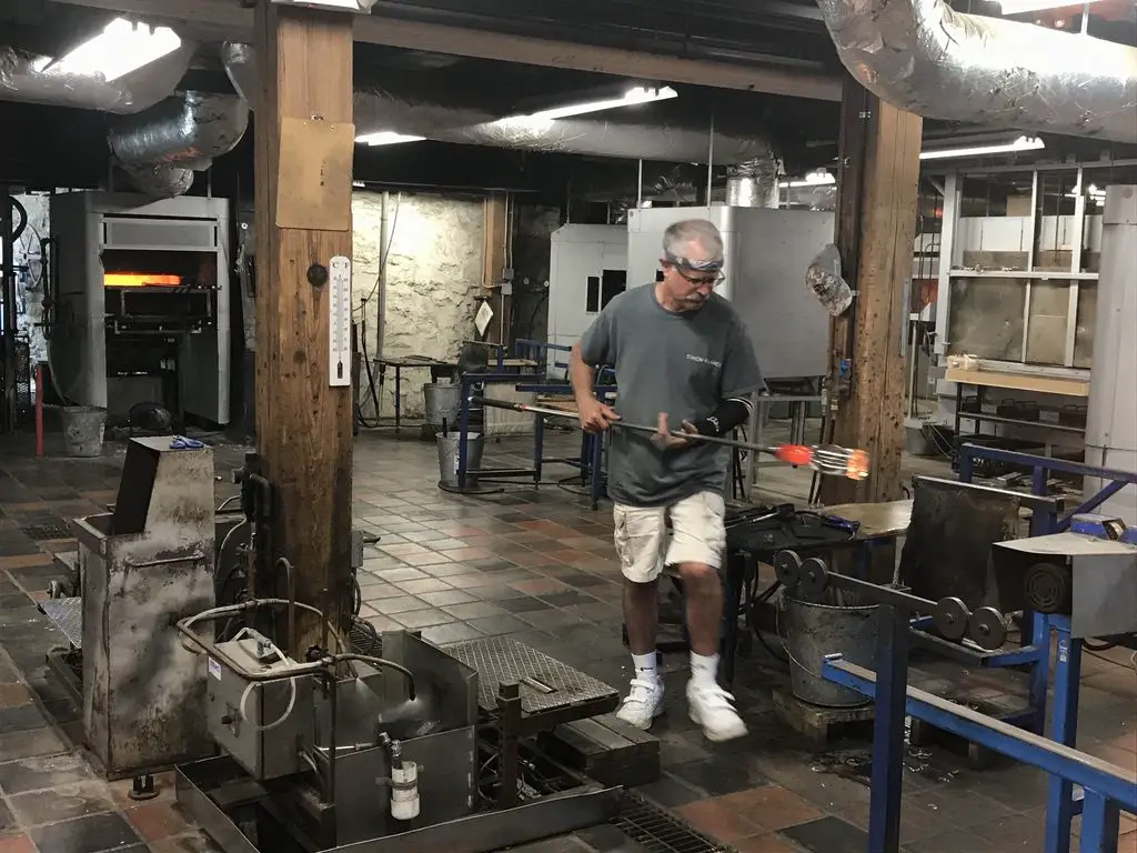 A glass blower crafts red-hot, liquid glass in a workshop