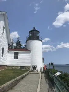 A white building and lighthouse. A bell sits in front of the lighthouse tower