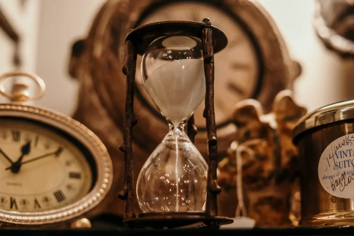 Brown-tinged photo or a wooden hourglass with sand running through it. A variety of clocks are in the background.