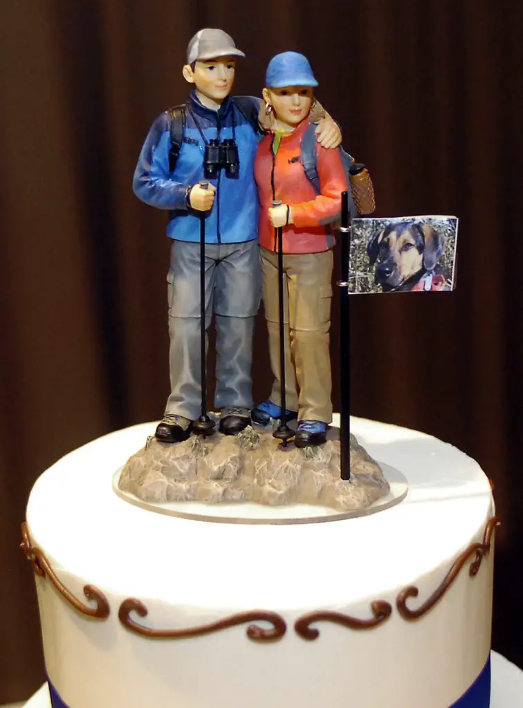 A cake topper with a male and female in hiking clothes/equipment and a flag with a picture of a dog