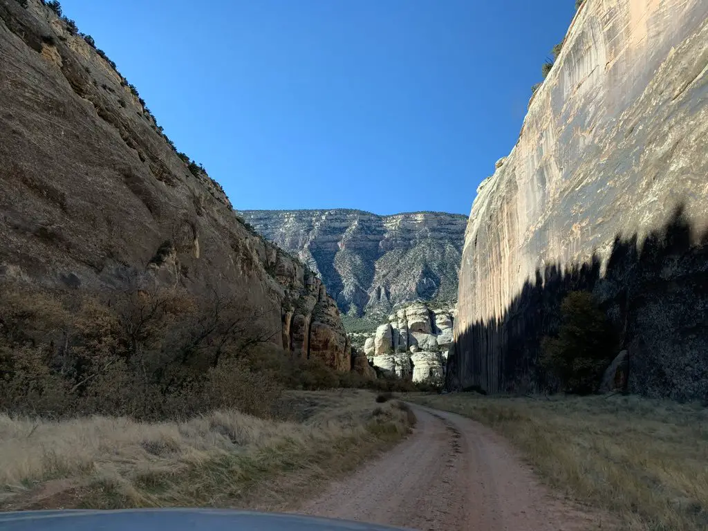 A dirt road snakes through a narrow canyon, rock towers on three sides.