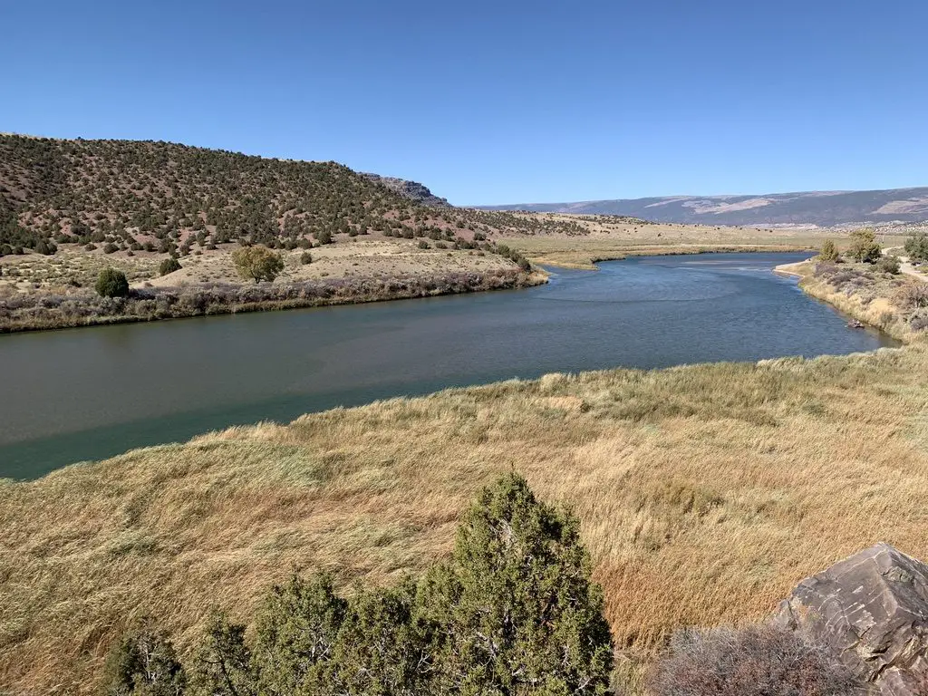 A river snakes through a desert landscape with yellow-grass meadows and scrub brush-covered hillsides