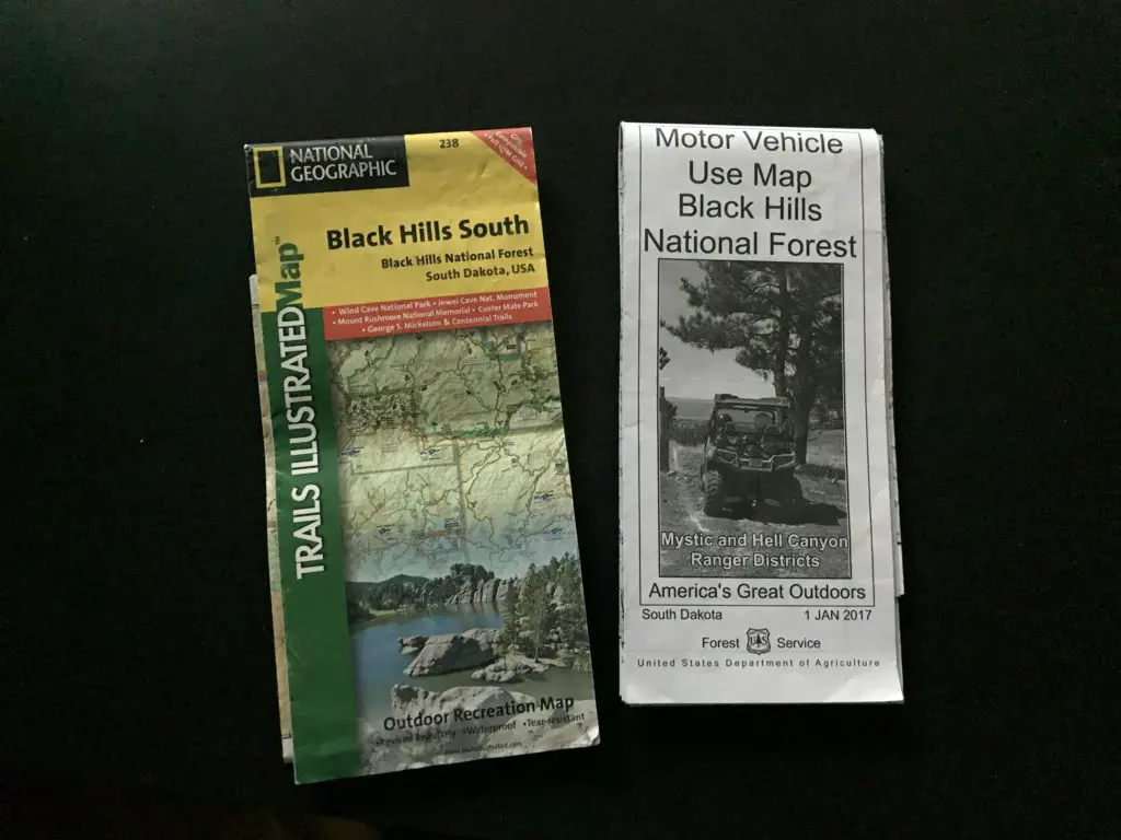 Two trail maps called "Black Hills South" and "Motor Vehicle Use Map Black Hills National Forest" sit against a black background