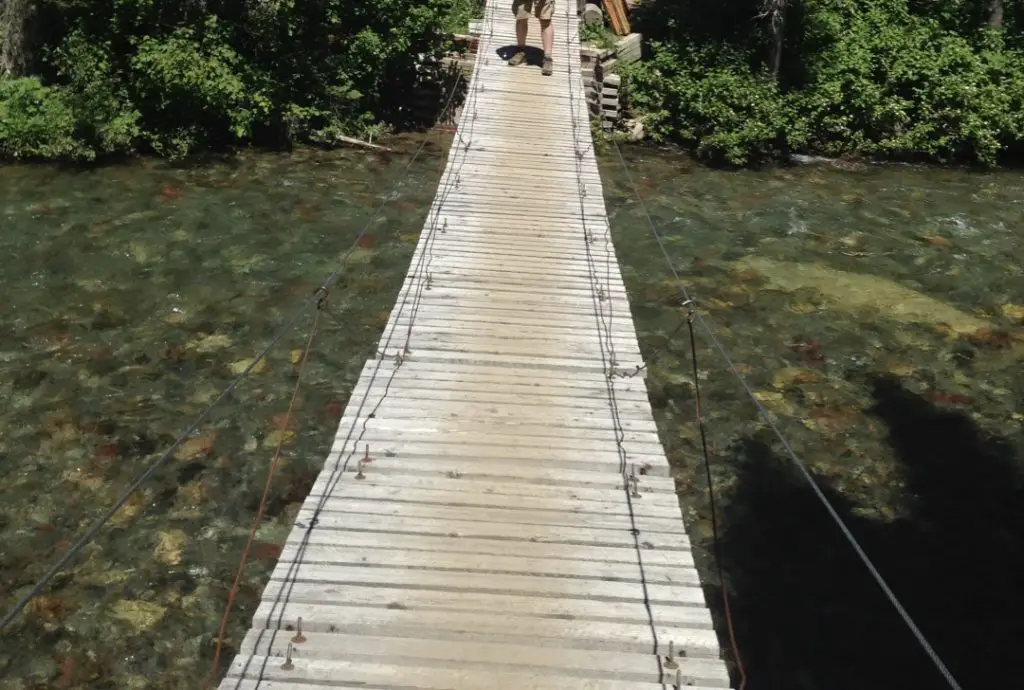 A wooden bridge with wires on the sides hangs over a river