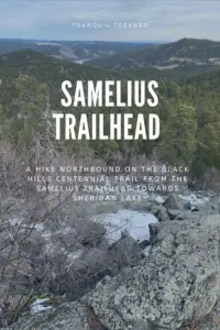 View over mountains covered in pine trees. In the foreground are rock boulders covered in a little snow. In the background, a tiny portion of a frozen lake peaks through the mountains. Pin reads, "Samelius Trailhead. A hike northbound on the Black Hills Centennial Trail from the Samelius Trailhead toward Sheridan Lake.