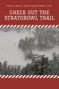 View from above of a snowy valley floor with the tops of pine trees covered in snow. A house sits in the middle of a meadow, The whole picture is obscured with flying snow. Pin reads, "For a quick hike near Rapid City check out the Stratobowl Trail"