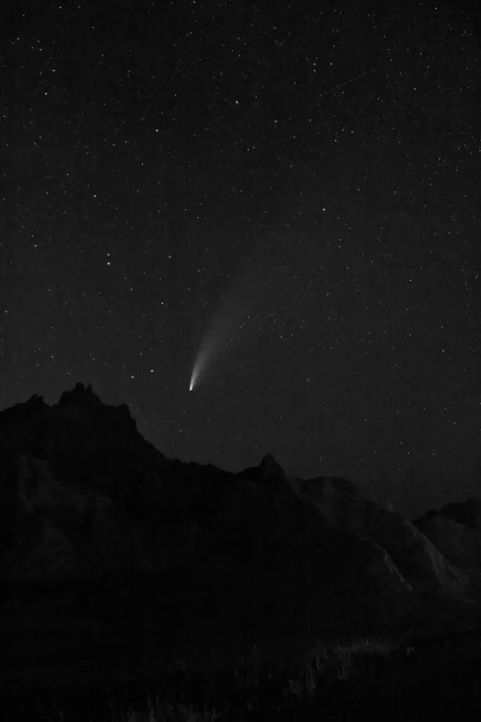 A small, white-colored comet streaks across the dark night sky
