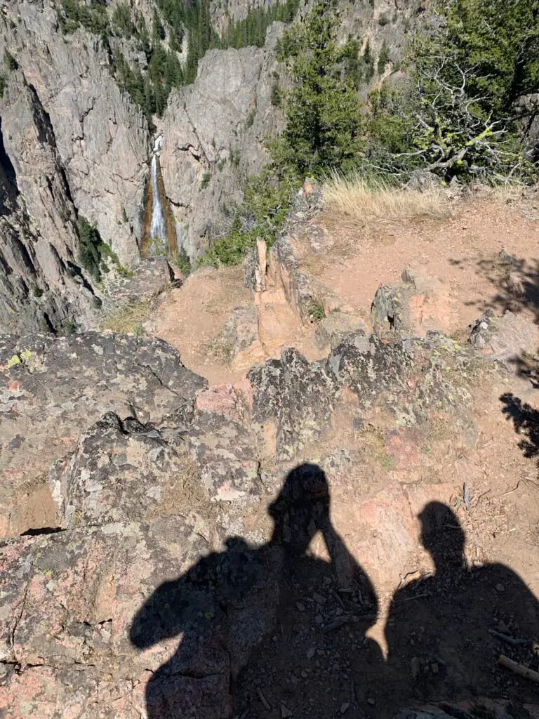 Shadows of two people on the rocky ground with a waterfall cascading down a rock wall in the background