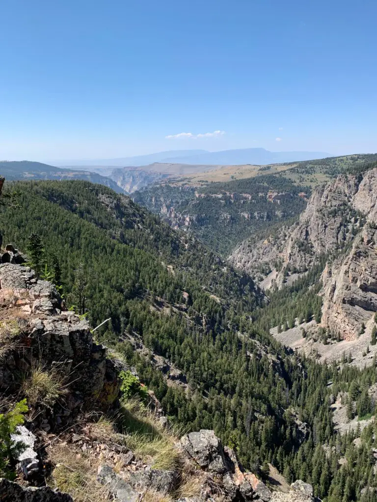 Tree-covered and rocky canyon walls. Taller mountains loom through the haze in the distance