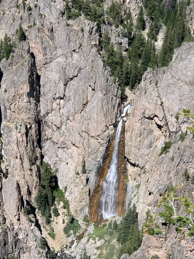 Viewed from above, a large, thin waterfall cascades down a rock wall 