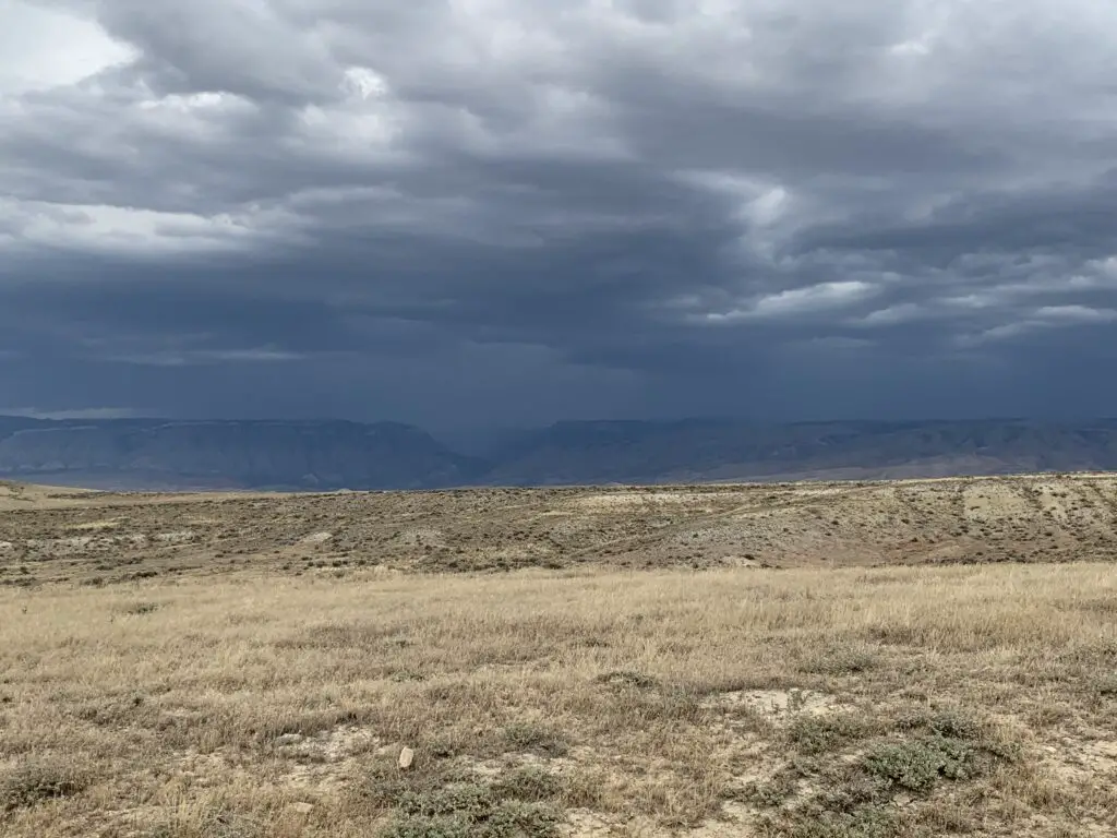 Dry, dusty prairie with dark rain clouds hovering over the landscape in the background