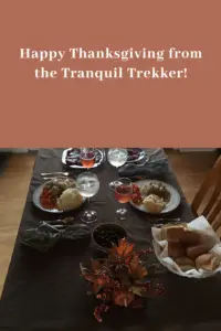 Picture of a table set with food such as potatoes, carrots, rolls, turkey and stuffing spread over it. Pin reads, "Happy Thanksgiving from the Tranquil Trekker!"