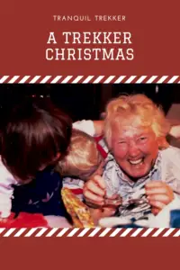 A grandma lays on the floor laughing and playing with two grandchildren amongst wrapping paper. Pin reads, "A Trekker Christmas"