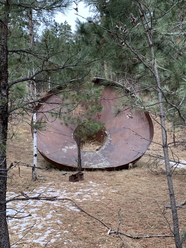 A very large, rusty, metal funnel sits in the woods