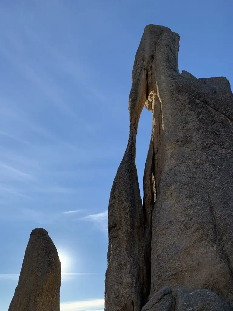 Two large, rock structures, one with a long, narrow hole, all under a blue sky.