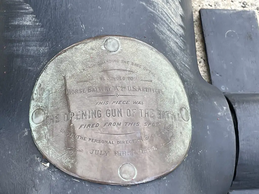 A metal sign stuck to the side of a cannon that reads, "Opening gun of the battle fired from this spot"