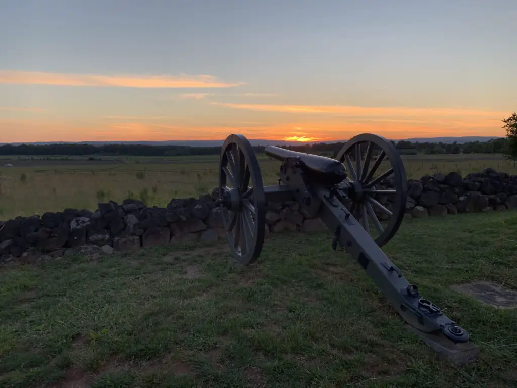 A cannon sits on a hill, overlooking a field at sunset