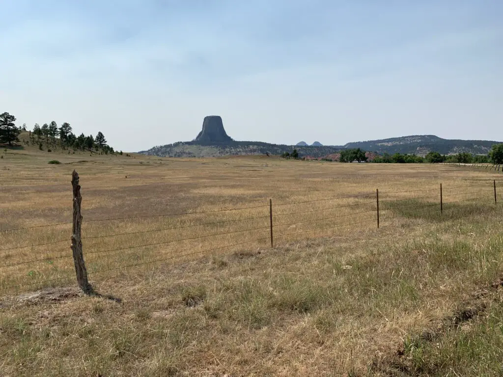 A brown-grass meadow leads to a rocky monolith (Devils Tower) in the distance. 