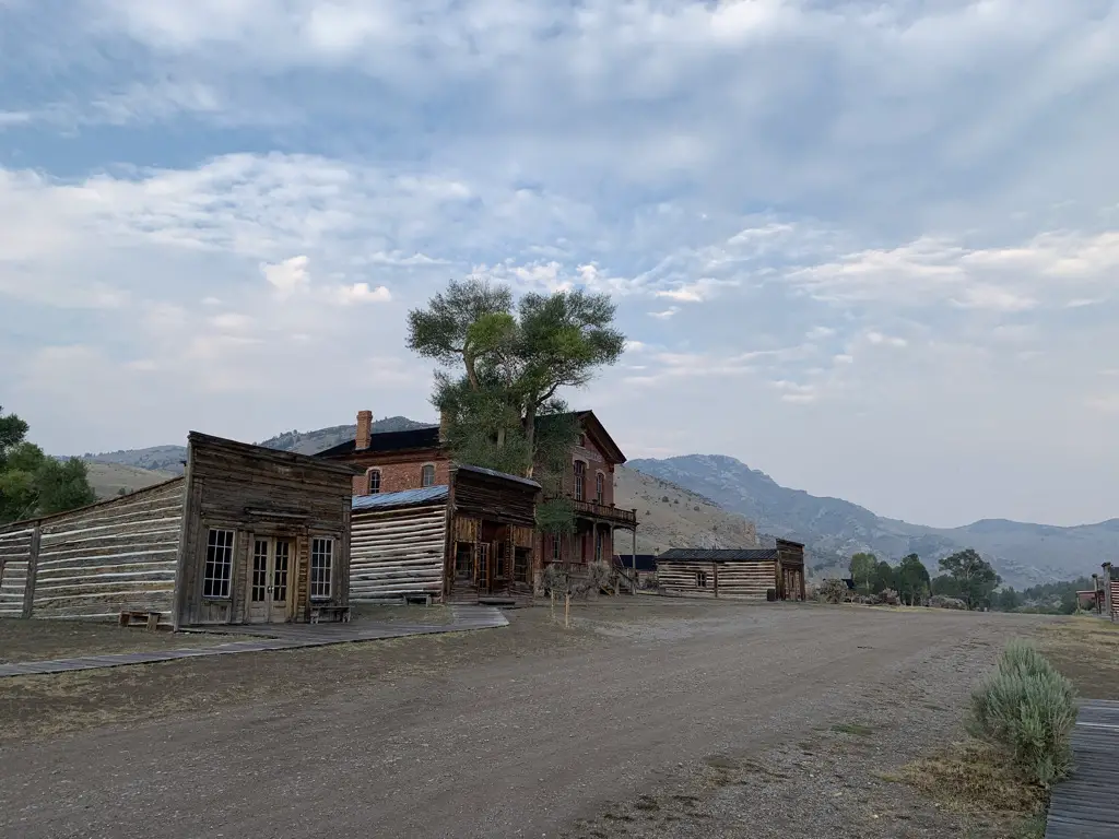 Old, wooden buildings line one side of dirt, street.