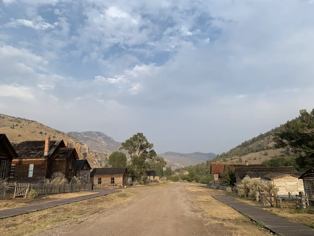 View down dirt, main street of Bannack ghost town, Bannack State Park. Old, wooden buildings on each side, blue, cloud-covered sky, dusty mountains in background..