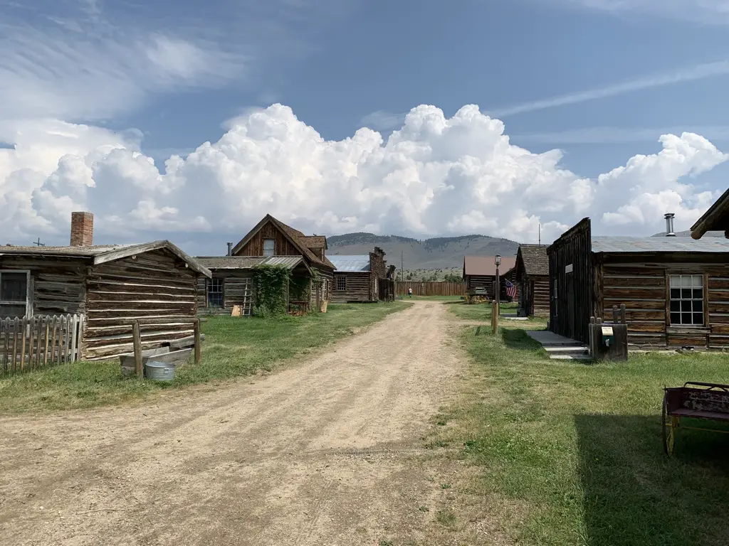 View down dirt street of a ghost town. Old, wooden buildings on each side. Blue sky with clouds