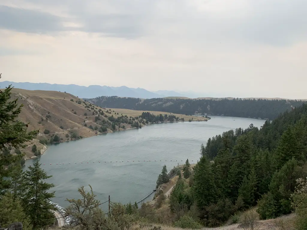 A river flows through a valley surrounded by tree-covered hillsides with dark mountains in the background