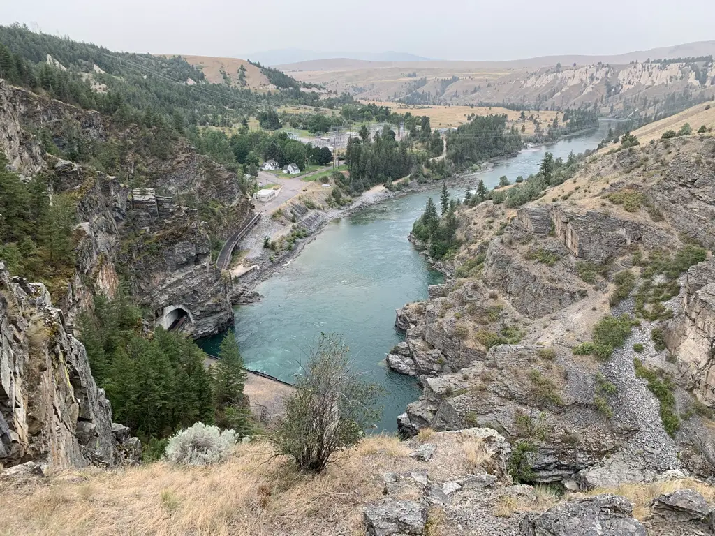 A river flows through a valley surrounded by rugged, rocky and tree-covered hillsides