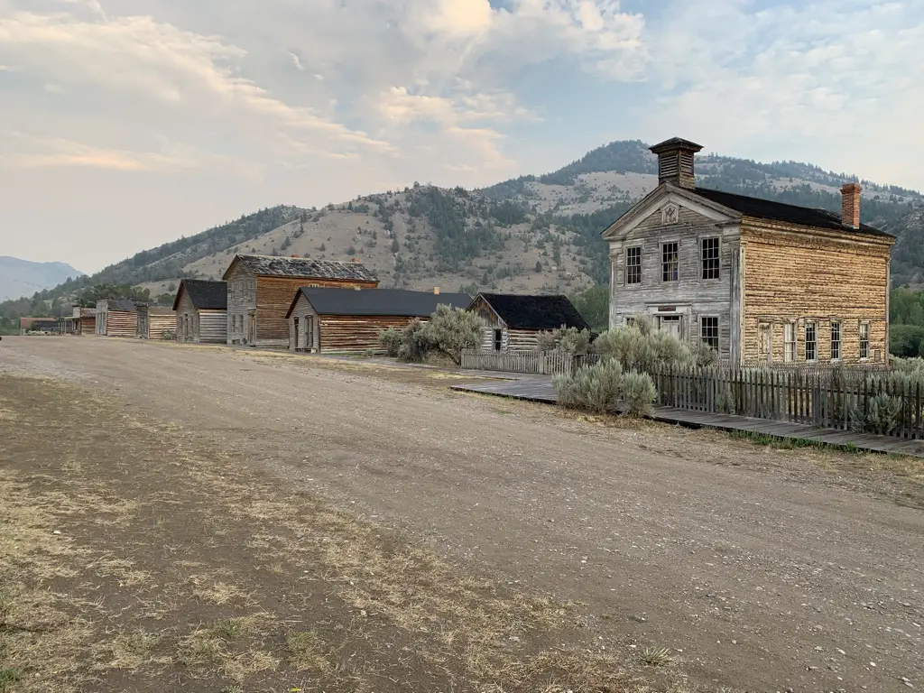 Old, wooden buildings line one side of dirt, street.