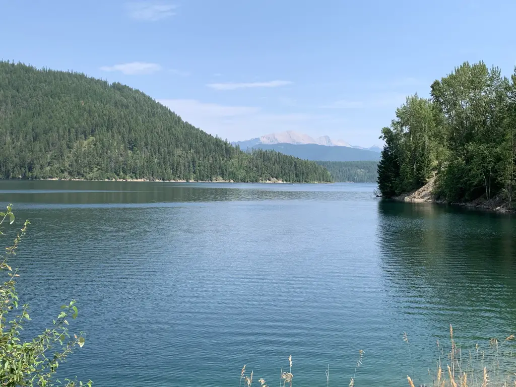 A serene lake surround by forested mountains. A large, rocky mountain looms in the background.