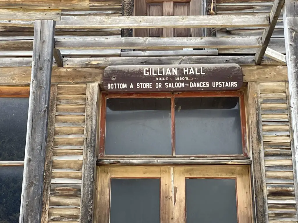 Front of old, wooden building. Sign says, "Gillian Hall: Built 1880's, Bottom a store or saloon, dances upstairs."