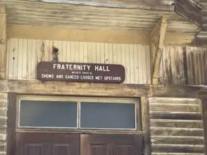 Front of old, wooden building. Sign says, "Fraternity Hall, shows were upstairs"