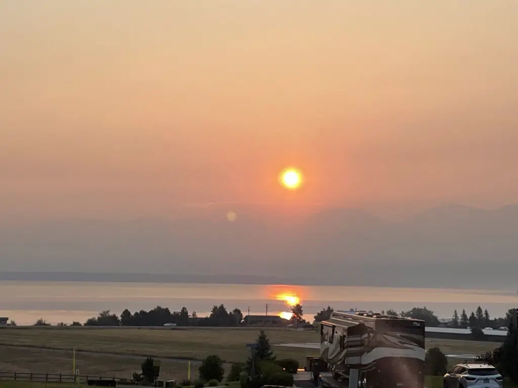 Sun shines through the haze of wildfire smoke and is reflected on the water of a lake