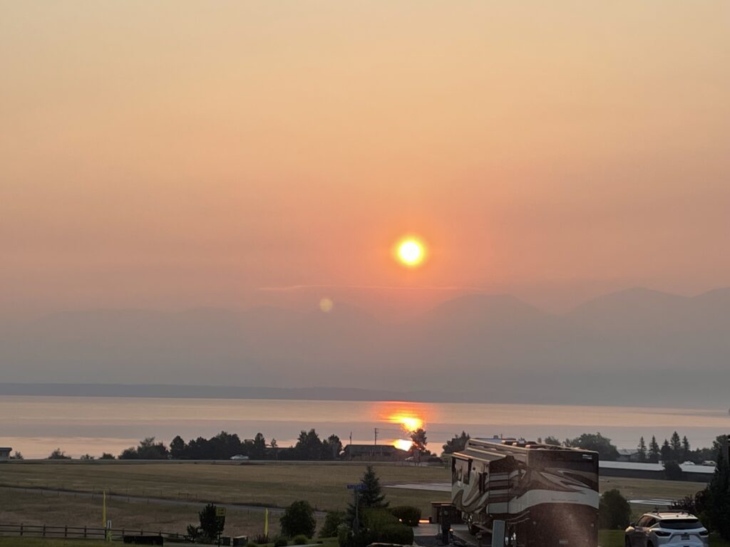 Sun shines through the haze of wildfire smoke and is reflected on the water of a lake