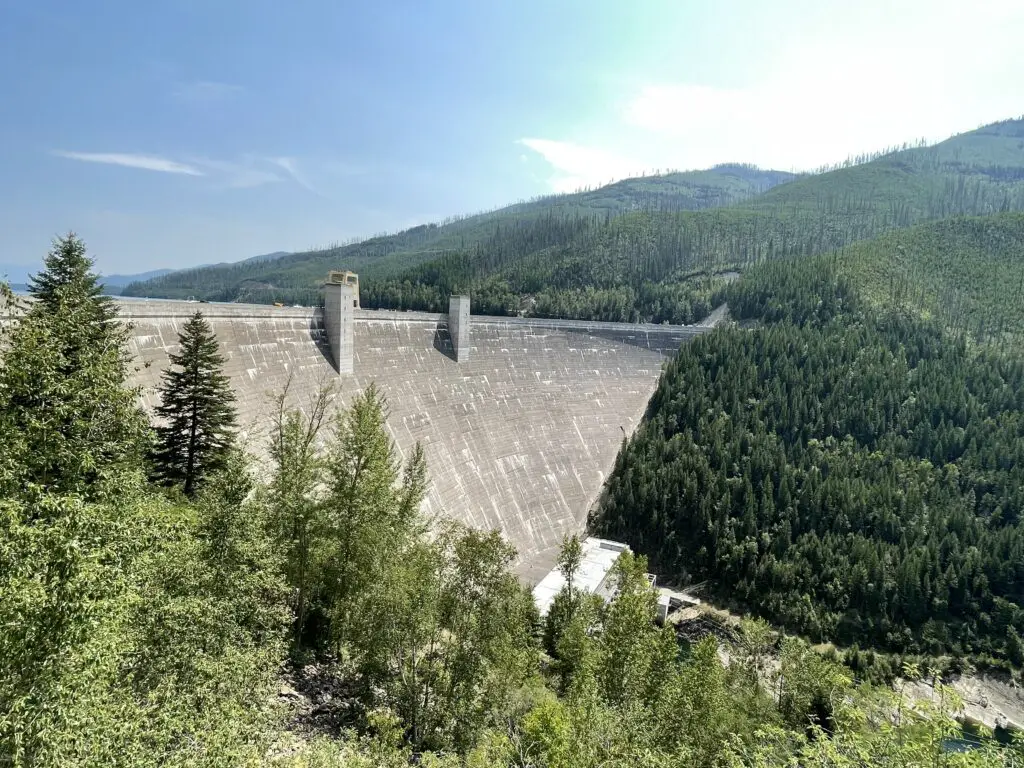 Large, concrete dam sits in the middle of forested mountains
