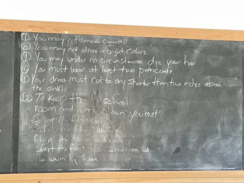 Rules for teachers at the schoolhouse in 1915 written on a chalkboard, including, "you may not dress in bright colors."