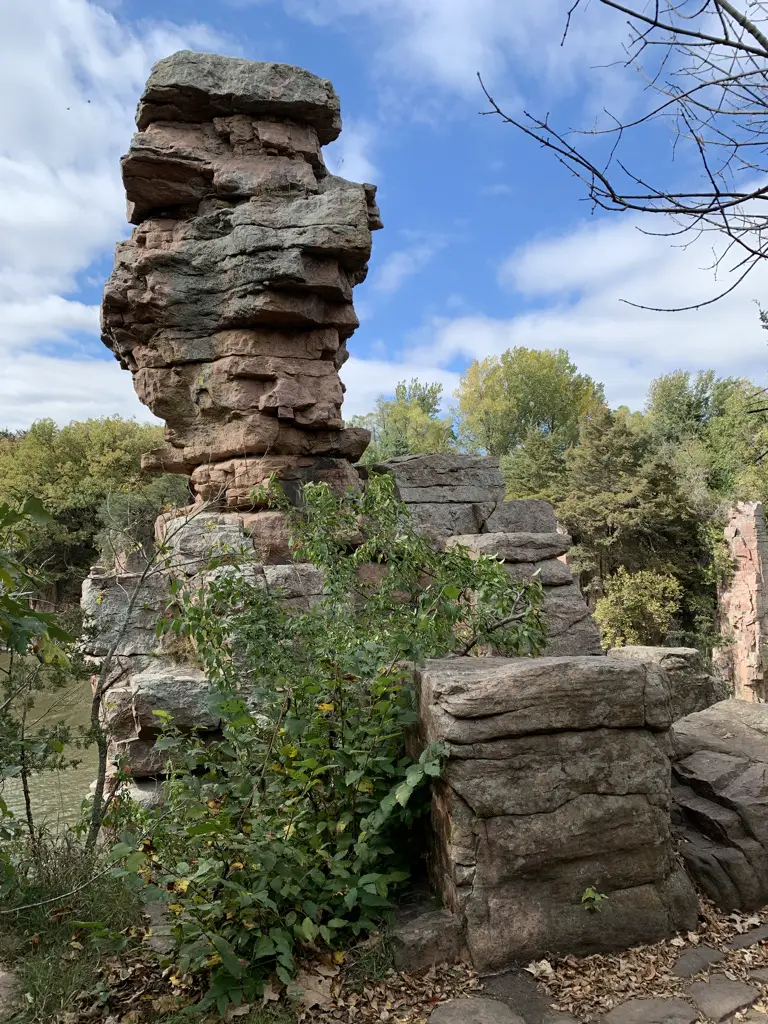 Towering rock formation, green vegetation and cloud-filled, blue sky in background.