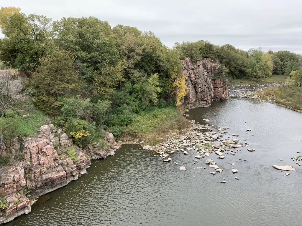 Creek in foreground, vegetation-covered rock walls in background, grey, cloudy sky.