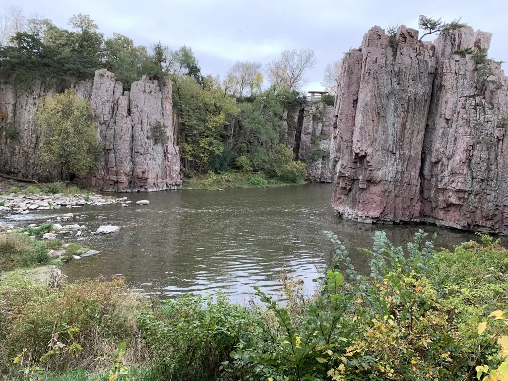 Creek running between a large break in a rock wall. Green vegetation tops the rocks and in foreground.